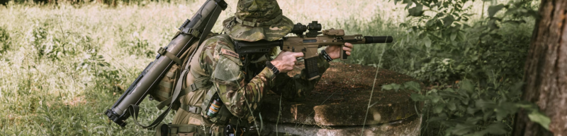 Airsoft player aiming gun while crouched in grass