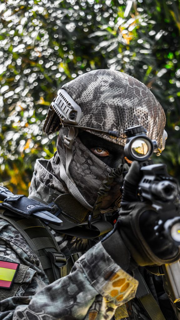 A person wearing black and grey camo and helmet holding an airsoft gun