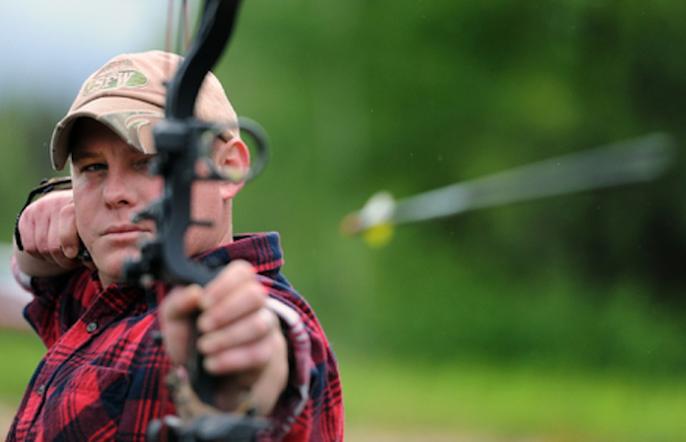 A man aiming and firing a crossbow