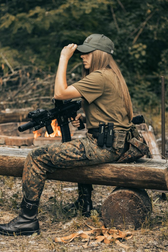 Woman sat on log in camo with airsoft gun