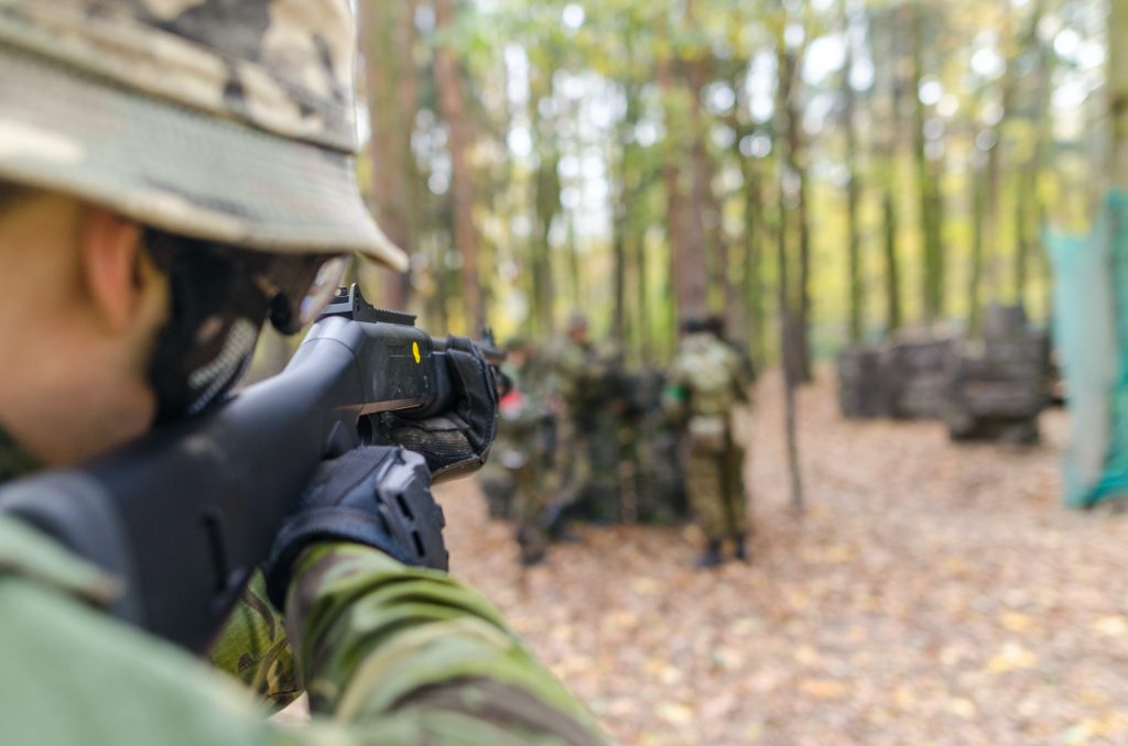 An airsoft player aiming a gun in the woods