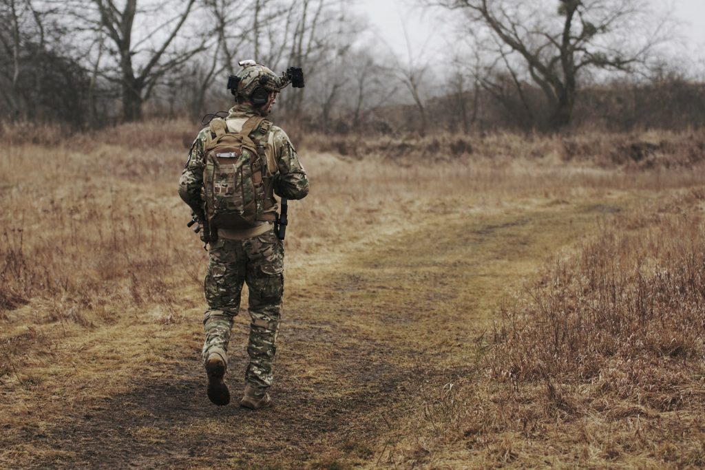 An airsofter in camo gear walking in a grassy field