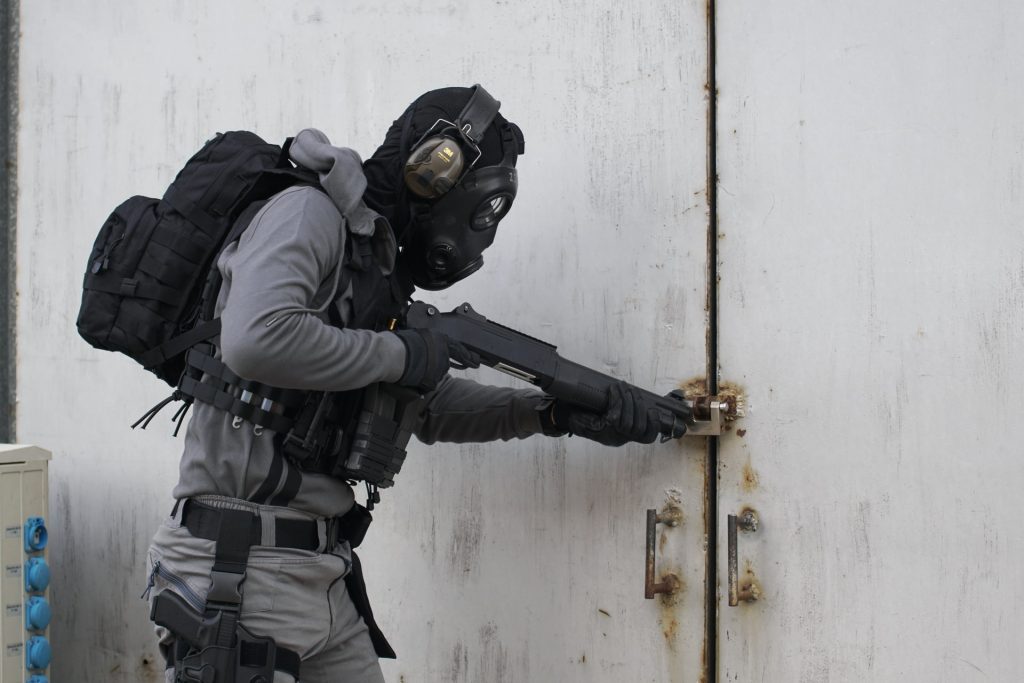 A person holding an airsoft gun and wearing a mask and ear defenders