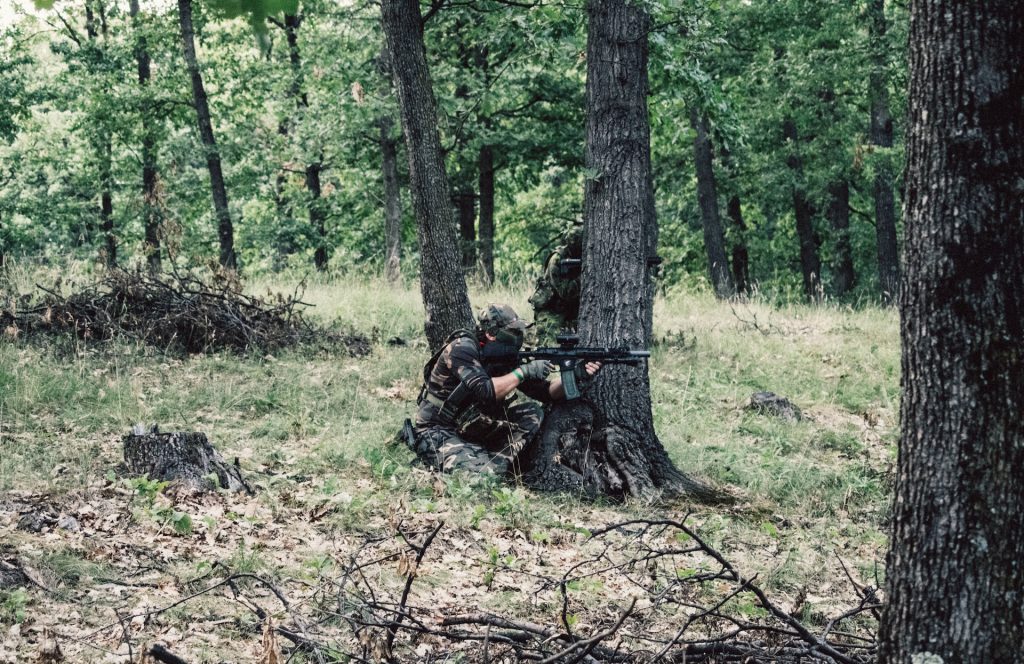 An airsoft player aiming a gun in the woods