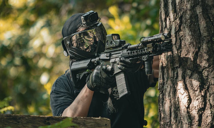 An airsoft player aiming a gun from behind a tree