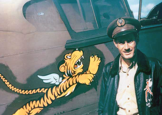 Flying Tigers pilot posing next to the insignia on a plane. 